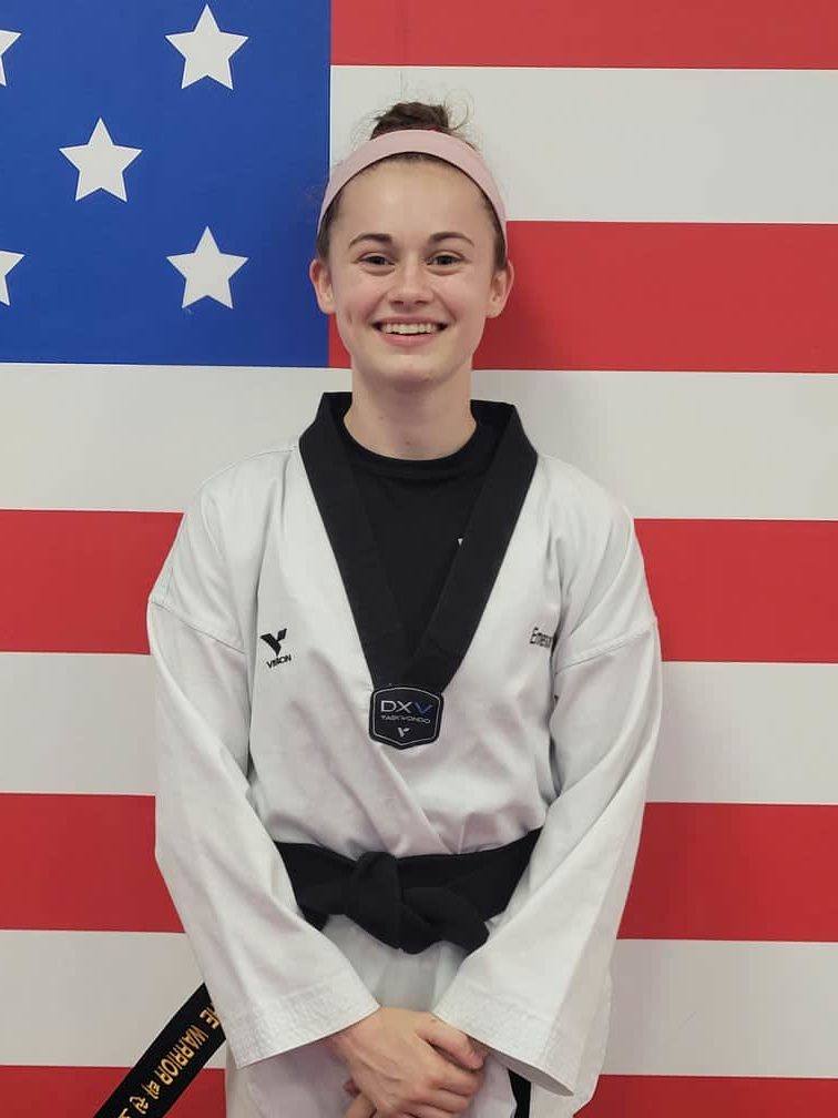 Caucasian teen girl wearing taekwondo dobak standing against a USA flag wall
